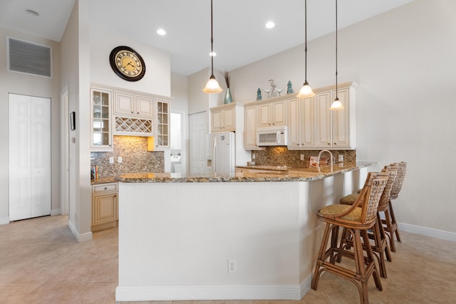 kitchen with cream cabinets, kitchen peninsula, light stone countertops, white appliances, and decorative light fixtures