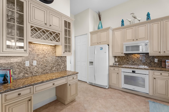 kitchen with dark stone countertops, white appliances, and cream cabinets