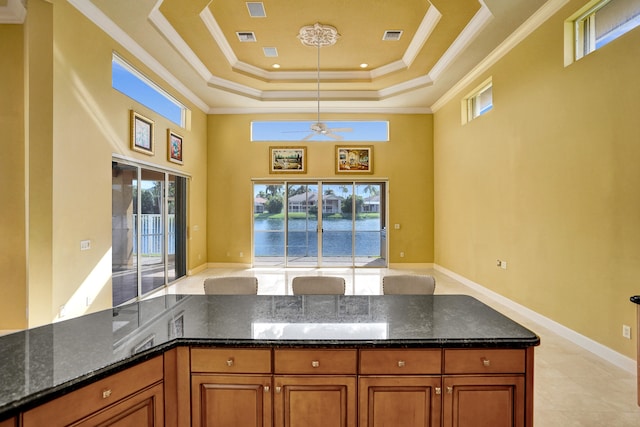 kitchen with ornamental molding, ceiling fan, a tray ceiling, decorative light fixtures, and dark stone countertops