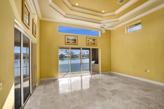 empty room with a tray ceiling, a water view, ornamental molding, and a towering ceiling