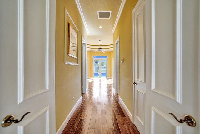 hallway with hardwood / wood-style floors, a textured ceiling, and ornamental molding