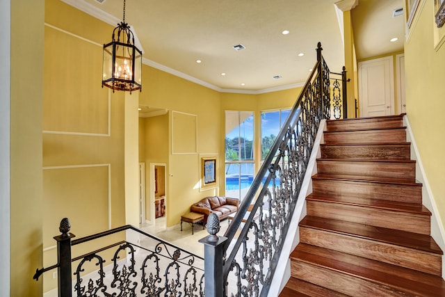 staircase with ornamental molding, hardwood / wood-style flooring, and an inviting chandelier