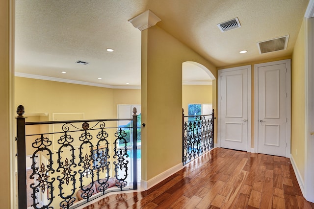 hallway featuring hardwood / wood-style floors, a textured ceiling, and ornamental molding