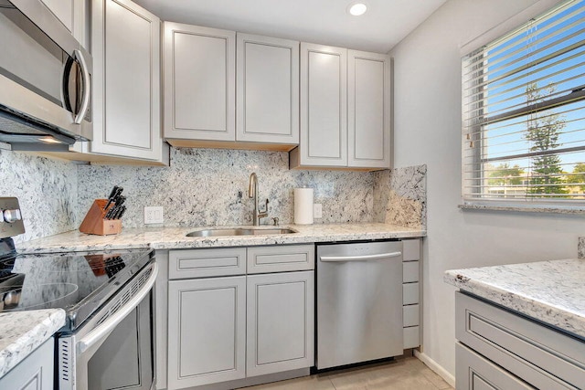 kitchen with sink, light stone counters, appliances with stainless steel finishes, light tile patterned floors, and backsplash