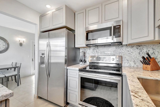 kitchen featuring appliances with stainless steel finishes, tasteful backsplash, light stone counters, and light tile patterned flooring