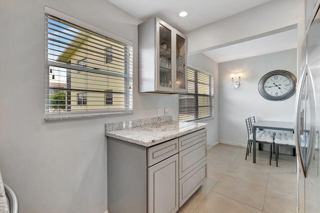 kitchen with plenty of natural light, light tile patterned floors, light stone counters, and stainless steel fridge