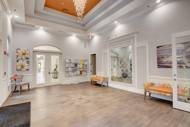 sitting room with a towering ceiling, wood-type flooring, a tray ceiling, and french doors