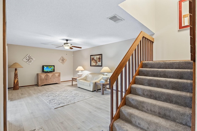 living room featuring ceiling fan, a textured ceiling, and light hardwood / wood-style flooring