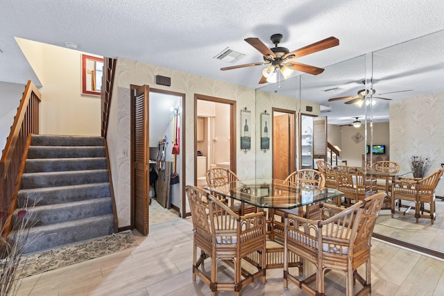 1904 SE Sir Lancelot Dr Unit 0, Port Saint Lucie, FL 34952 - dining space with wallpapered walls, ceiling fan, a textured ceiling, light wood-style flooring, and stairs
