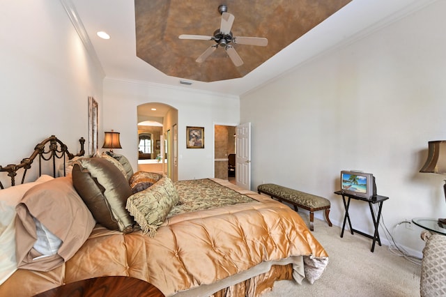 bedroom featuring light carpet, ensuite bath, ornamental molding, a tray ceiling, and ceiling fan