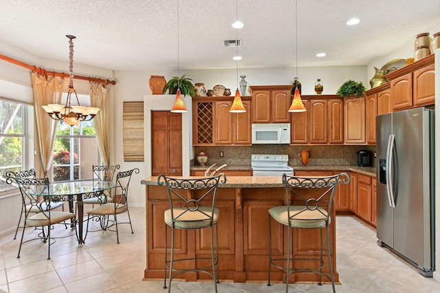 kitchen with white appliances, a center island with sink, a kitchen breakfast bar, decorative backsplash, and decorative light fixtures