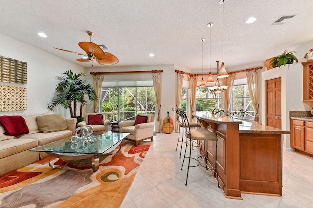 interior space featuring pendant lighting, ceiling fan with notable chandelier, a textured ceiling, and a breakfast bar