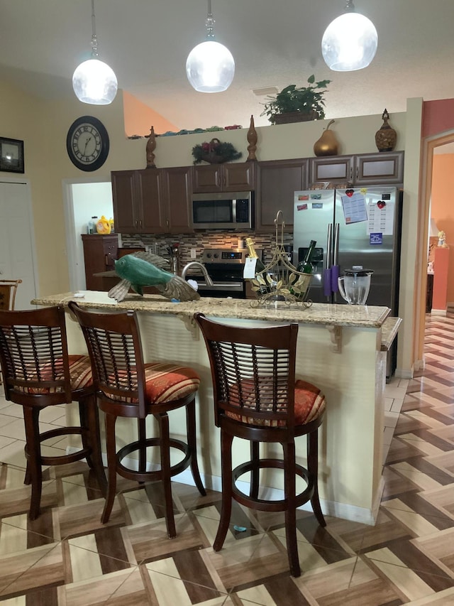 kitchen featuring a kitchen breakfast bar, decorative light fixtures, appliances with stainless steel finishes, dark brown cabinets, and light parquet flooring