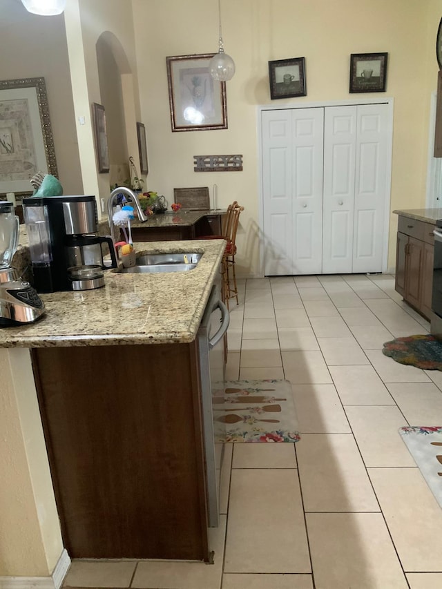 kitchen featuring pendant lighting, dishwasher, sink, light stone countertops, and light tile patterned flooring