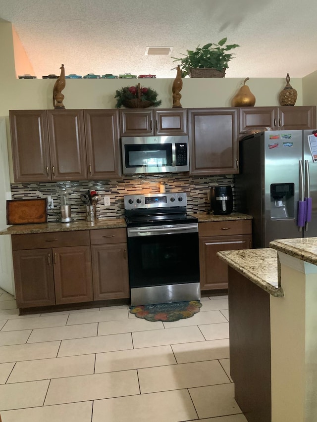 kitchen with light stone countertops, appliances with stainless steel finishes, a textured ceiling, and tasteful backsplash