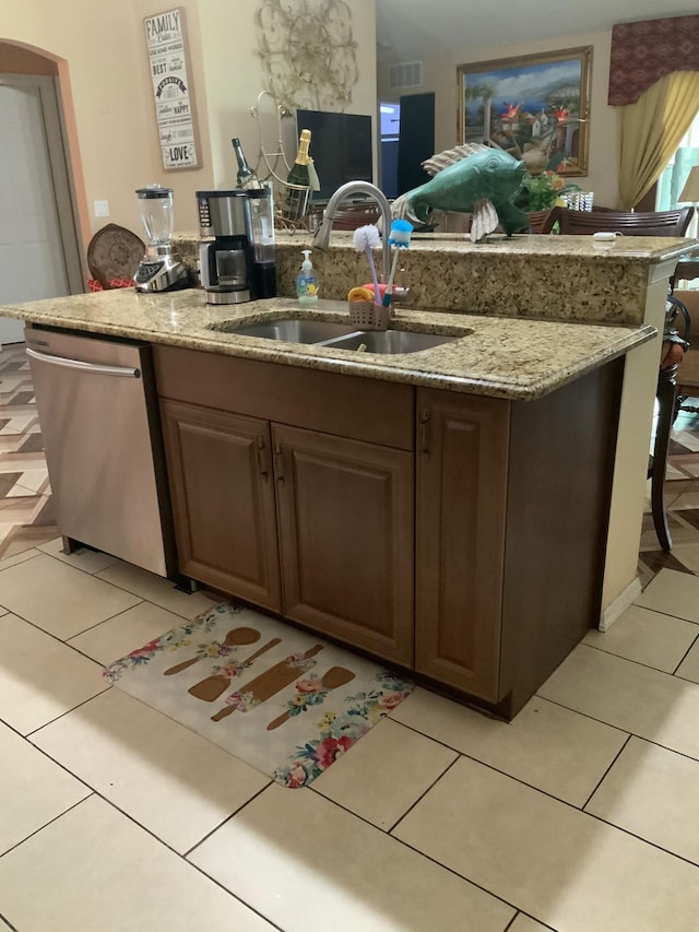 kitchen with sink, stainless steel dishwasher, light stone countertops, dark brown cabinets, and light tile patterned flooring