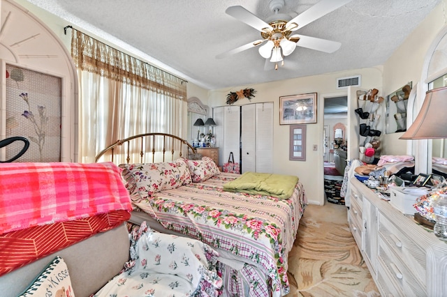bedroom featuring ceiling fan, light colored carpet, a textured ceiling, and a closet