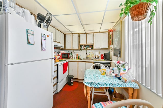 kitchen with a drop ceiling, dark carpet, white appliances, and sink
