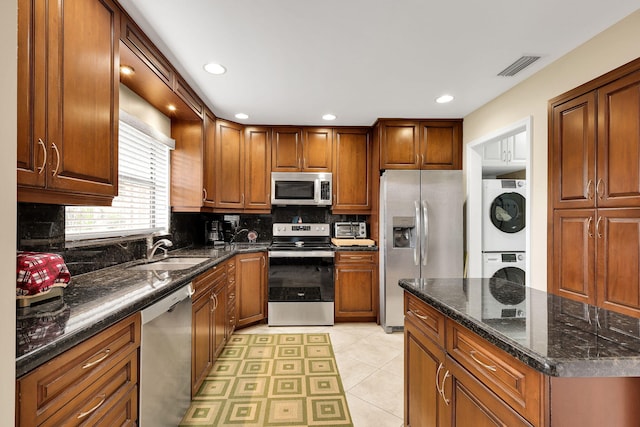 kitchen with stainless steel appliances, sink, tasteful backsplash, light tile patterned floors, and stacked washing maching and dryer