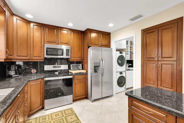 kitchen featuring appliances with stainless steel finishes, tasteful backsplash, stacked washer / dryer, and dark stone countertops