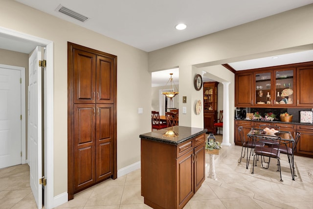 kitchen featuring dark stone counters, a kitchen island, decorative columns, and light tile patterned flooring