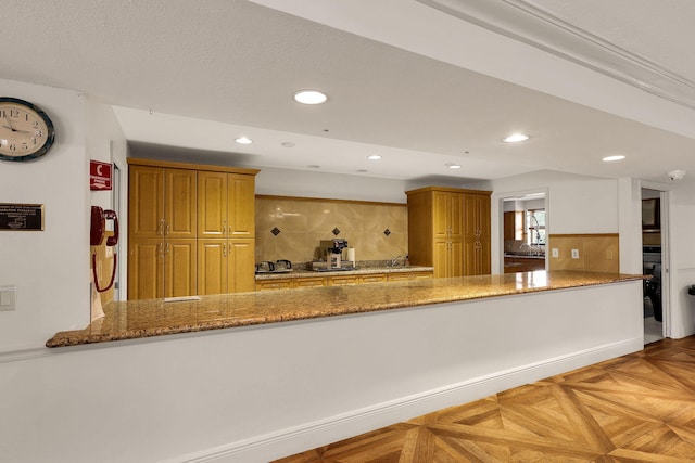 kitchen with light parquet floors, a textured ceiling, light stone counters, and kitchen peninsula