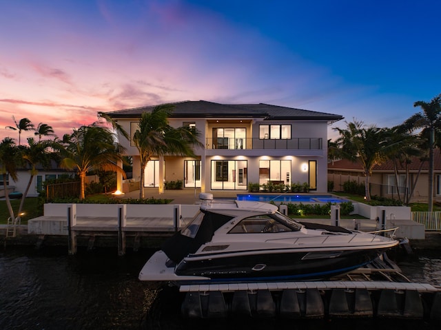 back of house at dusk featuring a patio, stucco siding, fence, a balcony, and an outdoor pool