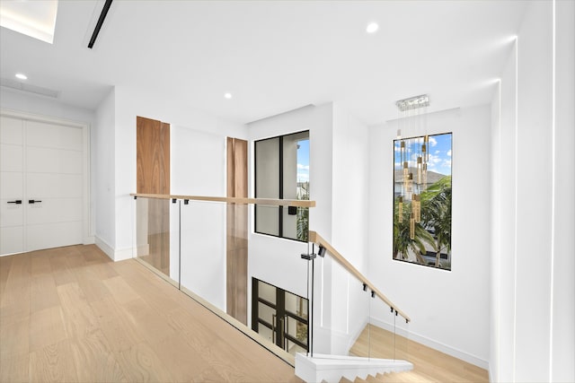 corridor with baseboards, light wood finished floors, an upstairs landing, and recessed lighting