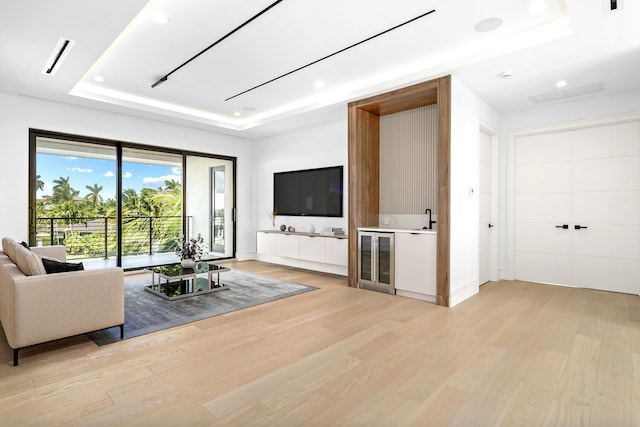 living area with beverage cooler, a tray ceiling, light wood-style flooring, and recessed lighting