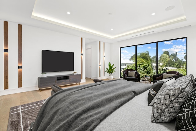 bedroom with access to exterior, a tray ceiling, wood finished floors, and recessed lighting