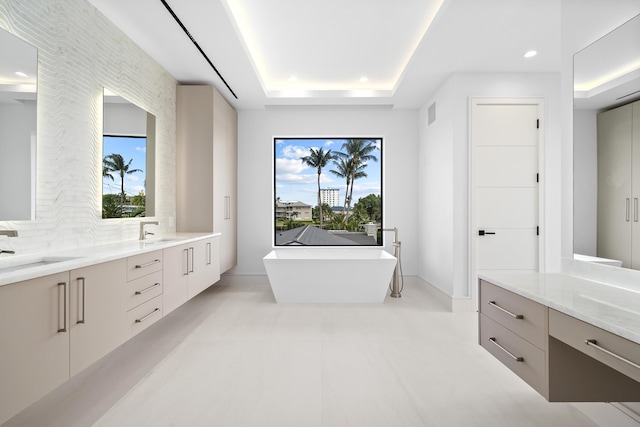 full bathroom featuring double vanity, a freestanding tub, a tray ceiling, and a sink