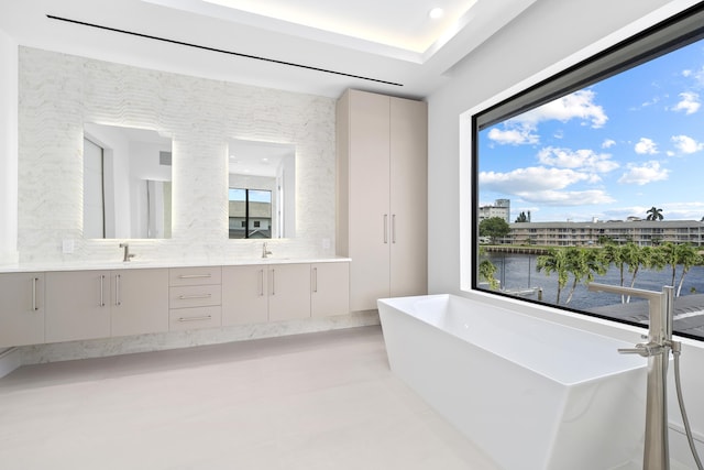 bathroom featuring double vanity, a freestanding tub, a healthy amount of sunlight, and a sink