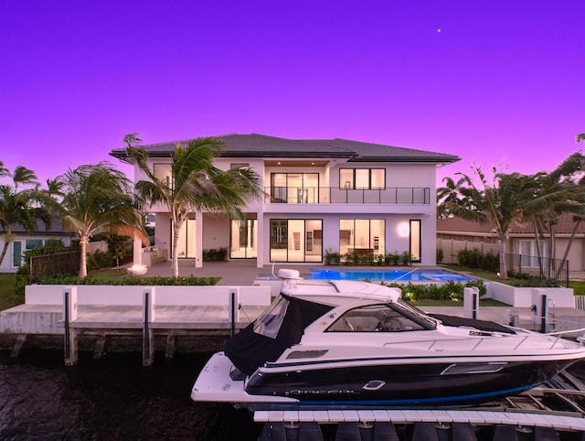 back of property at dusk with a patio, a balcony, fence, an outdoor pool, and stucco siding