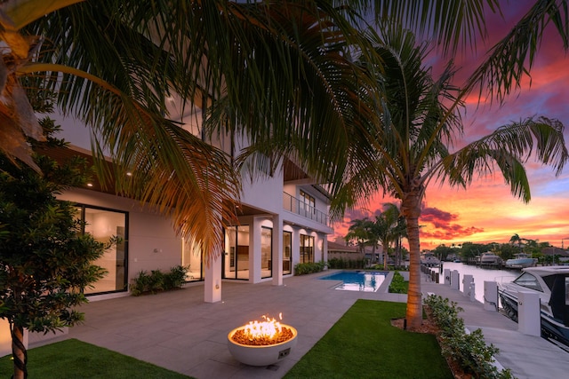 pool at dusk featuring a yard, a fire pit, an outdoor pool, and a patio