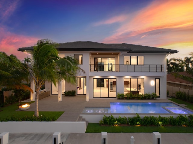 back of house at dusk featuring a fire pit, a patio, a balcony, a fenced backyard, and stucco siding