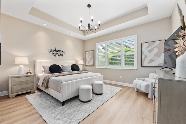 bedroom with an inviting chandelier, a tray ceiling, and light hardwood / wood-style flooring