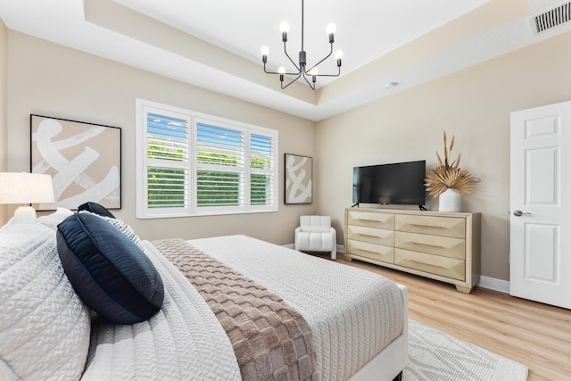 bedroom with a tray ceiling, light wood-type flooring, and an inviting chandelier