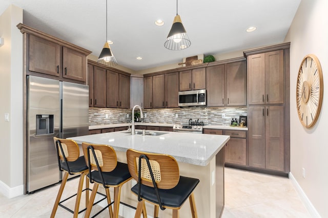 kitchen featuring pendant lighting, a kitchen island with sink, sink, light tile patterned floors, and appliances with stainless steel finishes