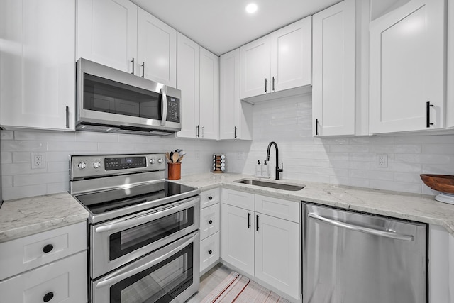 kitchen featuring light stone counters, stainless steel appliances, backsplash, white cabinetry, and sink