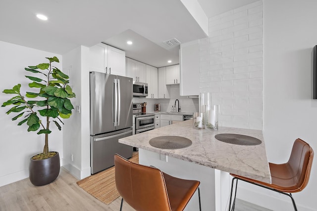 kitchen with stainless steel appliances, white cabinets, backsplash, light stone countertops, and light wood-type flooring