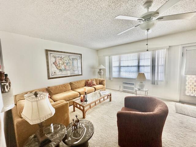 living room featuring ceiling fan, a wall mounted AC, a textured ceiling, and carpet floors