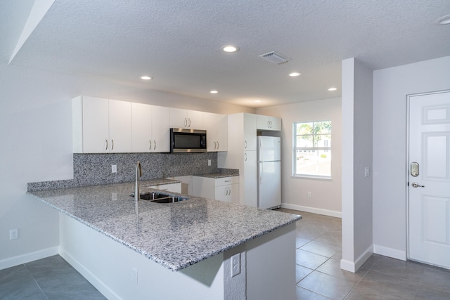 kitchen with white cabinets, kitchen peninsula, sink, backsplash, and white fridge