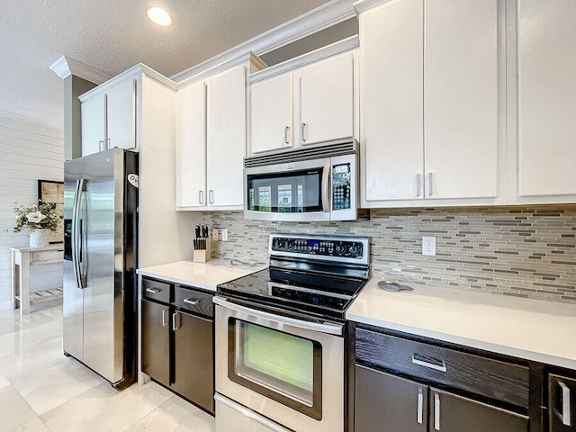 kitchen with appliances with stainless steel finishes, ornamental molding, a textured ceiling, light tile patterned floors, and white cabinets