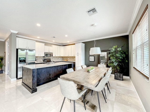 kitchen with stainless steel appliances, white cabinets, a center island with sink, and pendant lighting