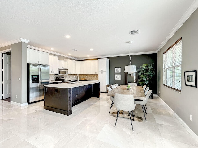 kitchen featuring appliances with stainless steel finishes, decorative light fixtures, sink, an island with sink, and white cabinets