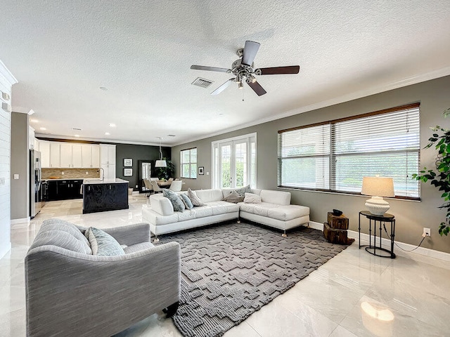 living room featuring ceiling fan, a textured ceiling, sink, and crown molding