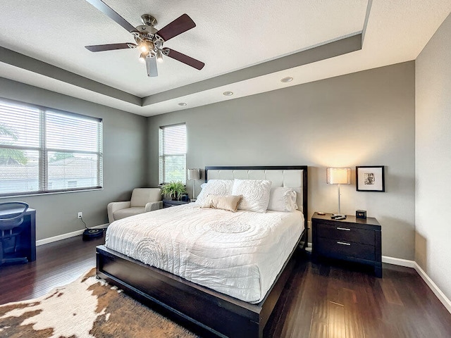 bedroom with a textured ceiling, dark hardwood / wood-style flooring, ceiling fan, and a raised ceiling