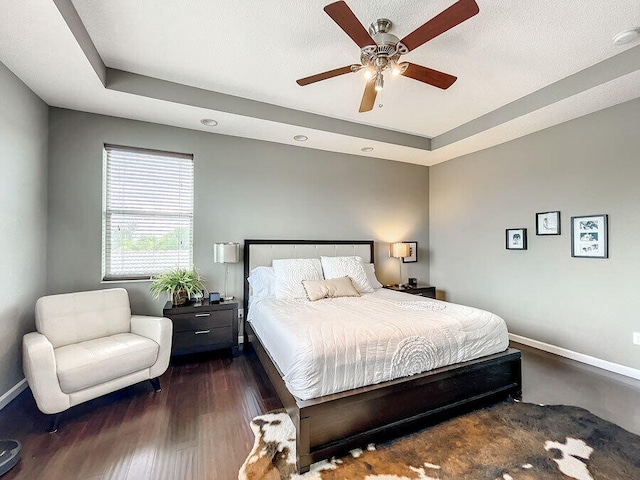 bedroom with dark hardwood / wood-style flooring, a tray ceiling, a textured ceiling, and ceiling fan