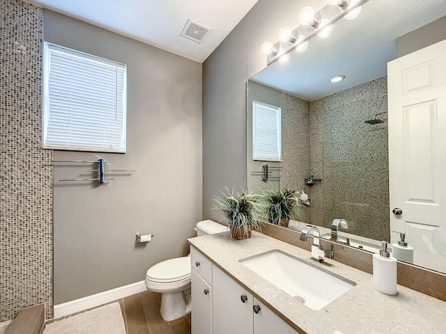 bathroom featuring toilet, vanity, hardwood / wood-style floors, and a tile shower