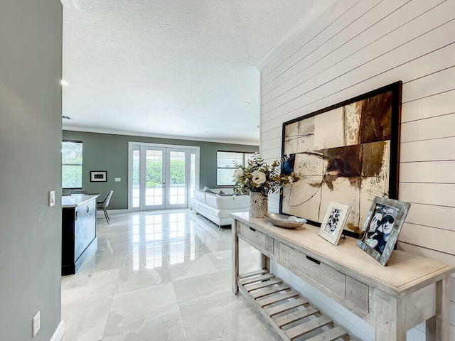 hallway with wood walls, a textured ceiling, crown molding, and french doors